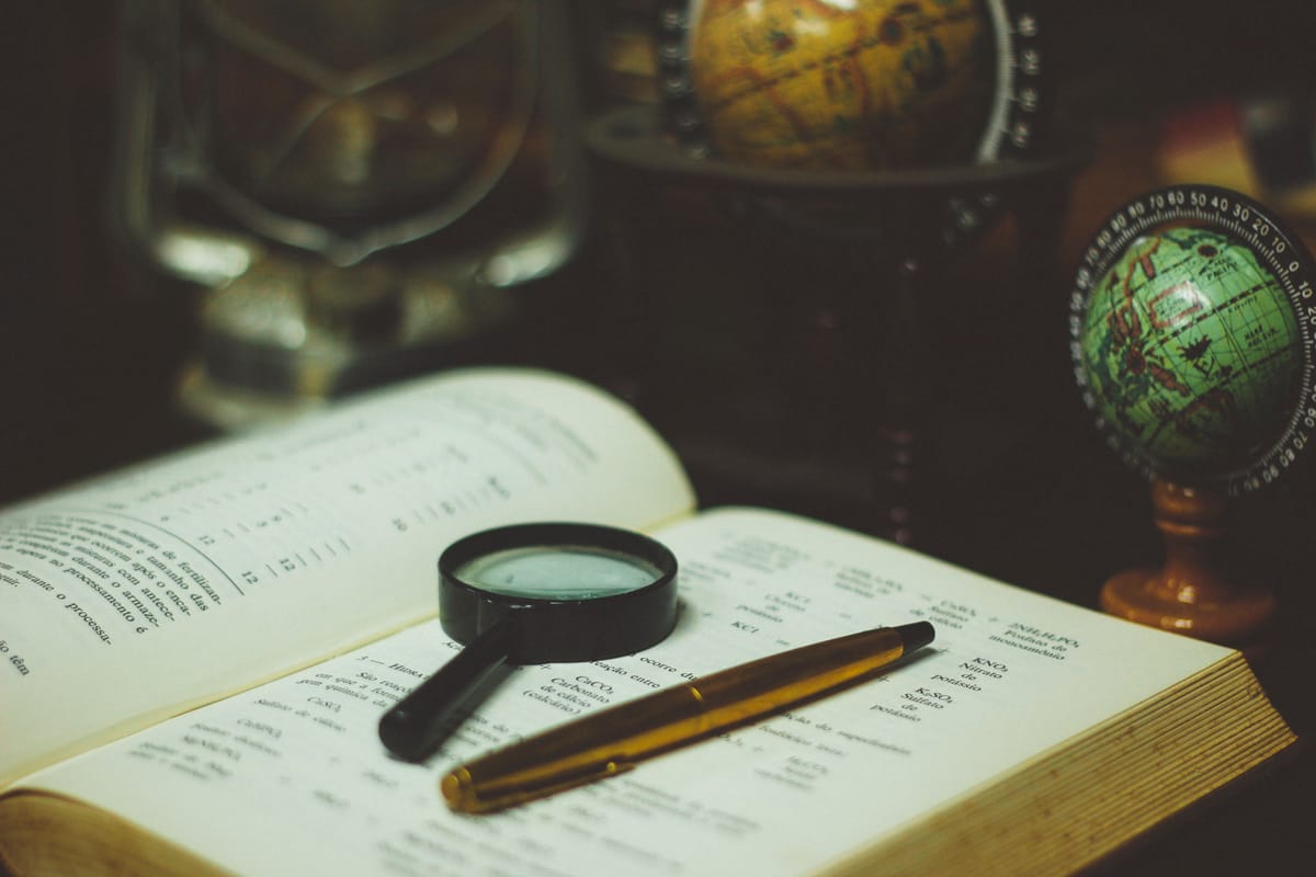 Une loupe et un stylo posés sur un livre ouvert, un petit globe terrestre à l'arrière-plan